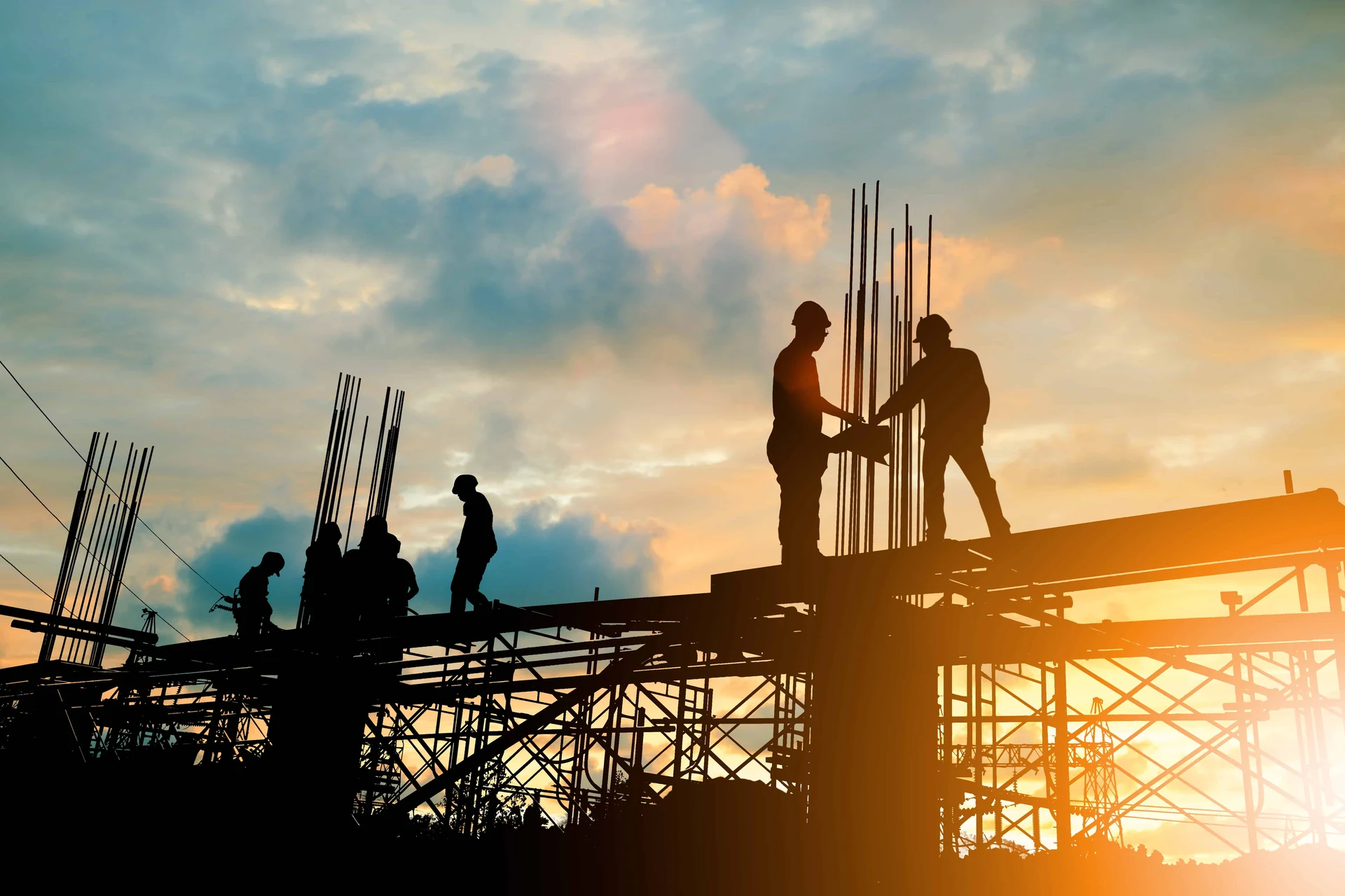 Construction workers silhouetted against a sunset at a building site